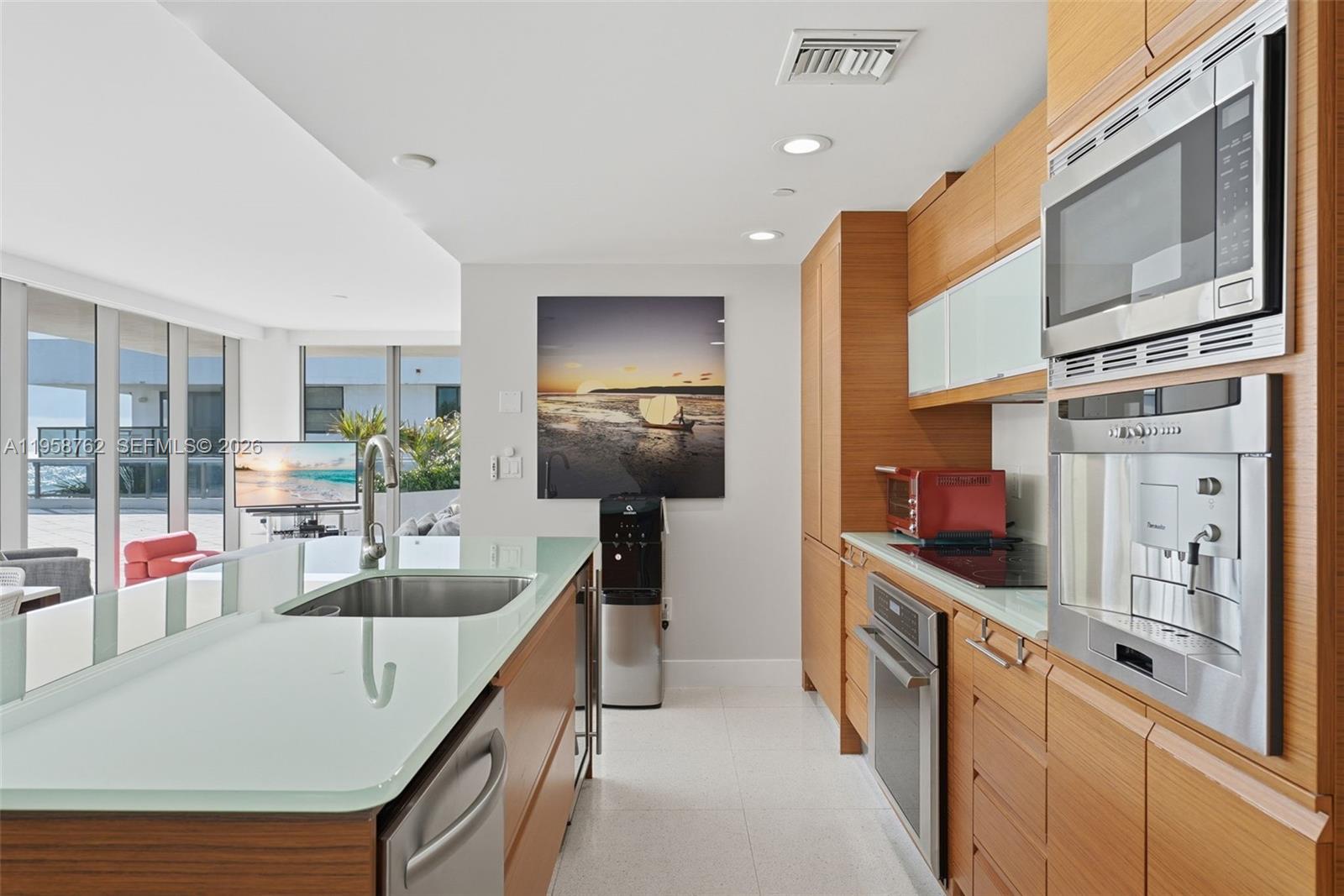 A modern kitchen features wood cabinetry, a glass-topped island, and stainless steel appliances — 5875 Collins Ave # 502, Miami Beach FL 33140, MIAMI BEACH, FL