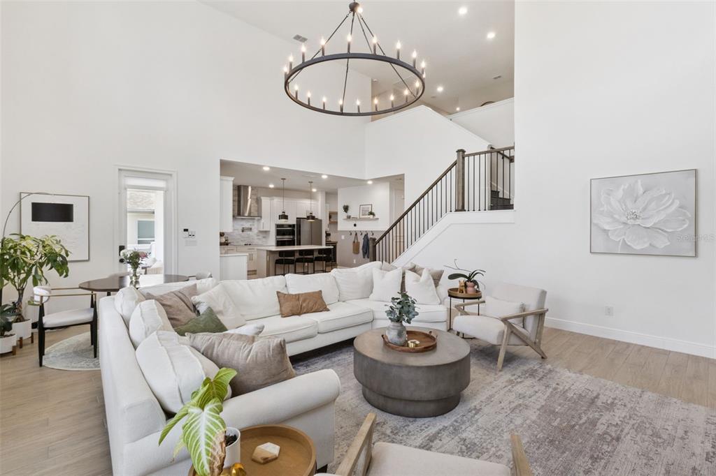 A bright, open-concept living room features a large sectional sofa, a chandelier, and a staircase — 2185 GOLD DUST DRIVE, MINNEOLA, FL