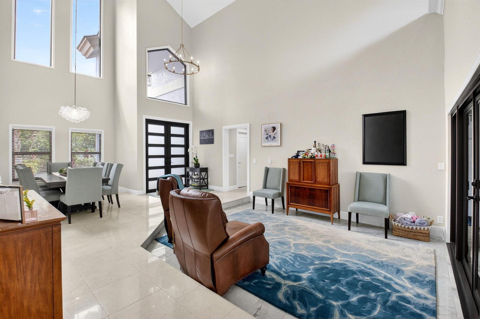 A high-ceilinged living and dining area features light tile floors, a blue rug, and furniture — 10655 Rio Hermoso, Delray Beach FL 33446, DELRAY BEACH, FL