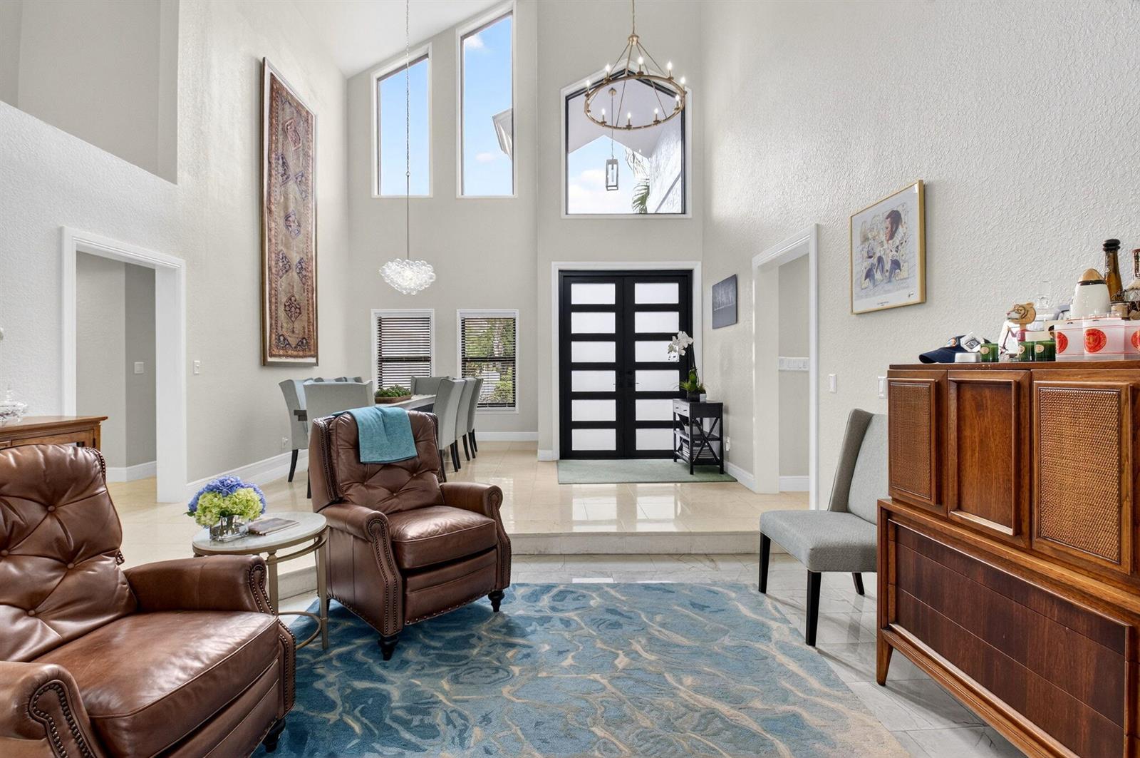 A high-ceilinged living and dining area features tile floors, leather armchairs, and a blue rug — 10655 Rio Hermoso, Delray Beach FL 33446, DELRAY BEACH, FL