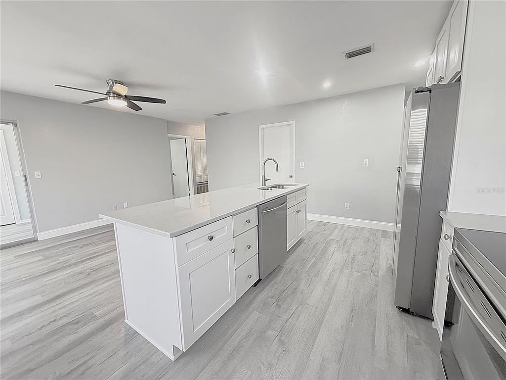 A kitchen features a white island with a sink, stainless steel appliances, and light flooring — 1231 ILLINOIS AVENUE UNIT 1, PALM HARBOR, FL
