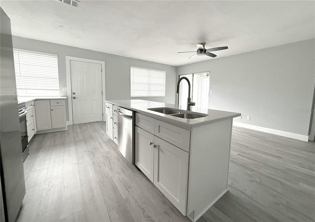 A kitchen features a central island with a sink, white cabinetry, and light wood flooring — 1231 ILLINOIS AVENUE UNIT 1, PALM HARBOR, FL