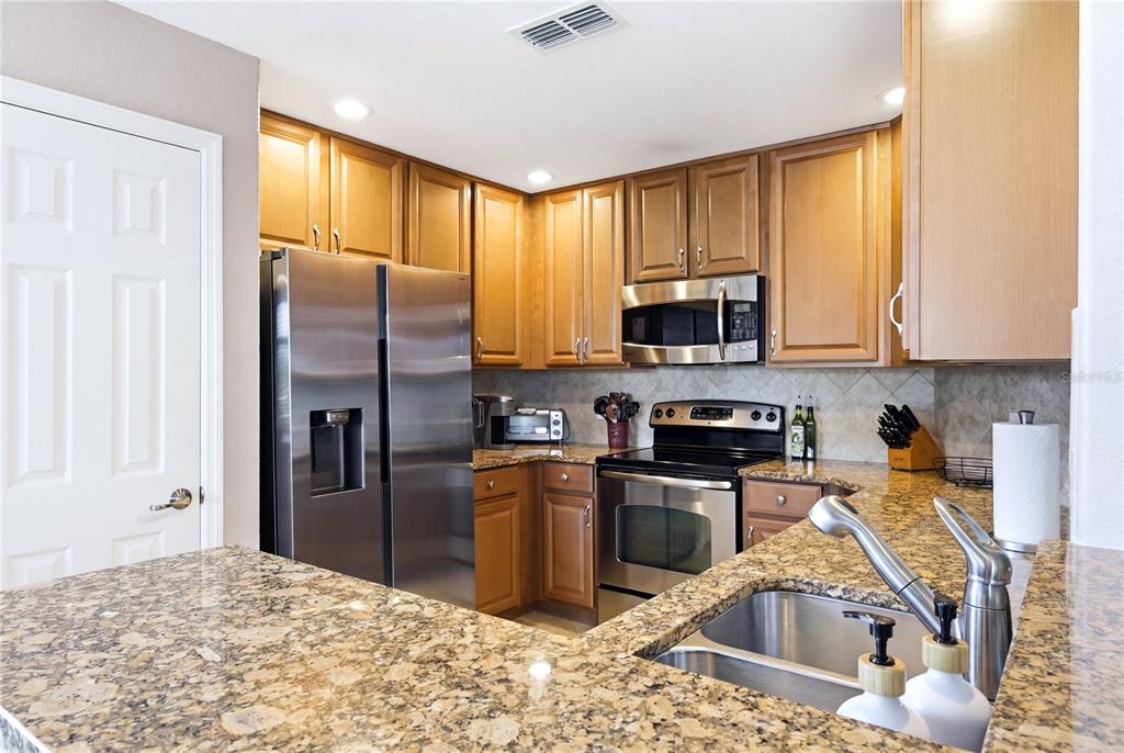 A kitchen features wood cabinets, granite countertops, stainless steel appliances, and a double-basin sink — 424 WINDING BROOK LANE UNIT 104, BRADENTON, FL