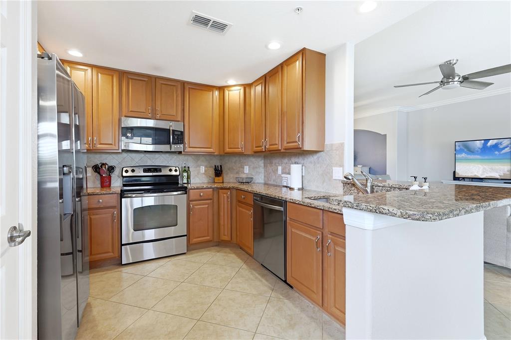 A kitchen features wood cabinets, granite countertops, stainless steel appliances, and tile flooring — 424 WINDING BROOK LANE UNIT 104, BRADENTON, FL