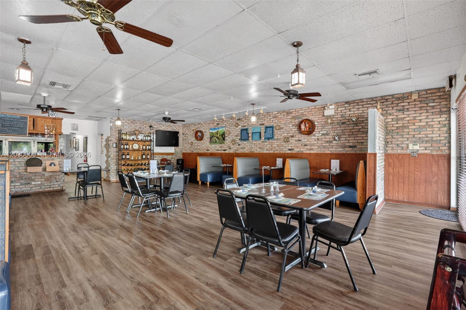 A restaurant dining room features brick walls, wood-look flooring, booth seating, and several tables — Turnkey Pompano Beach Restaurant, Pompano Beach FL 33060, POMPANO BEACH, FL