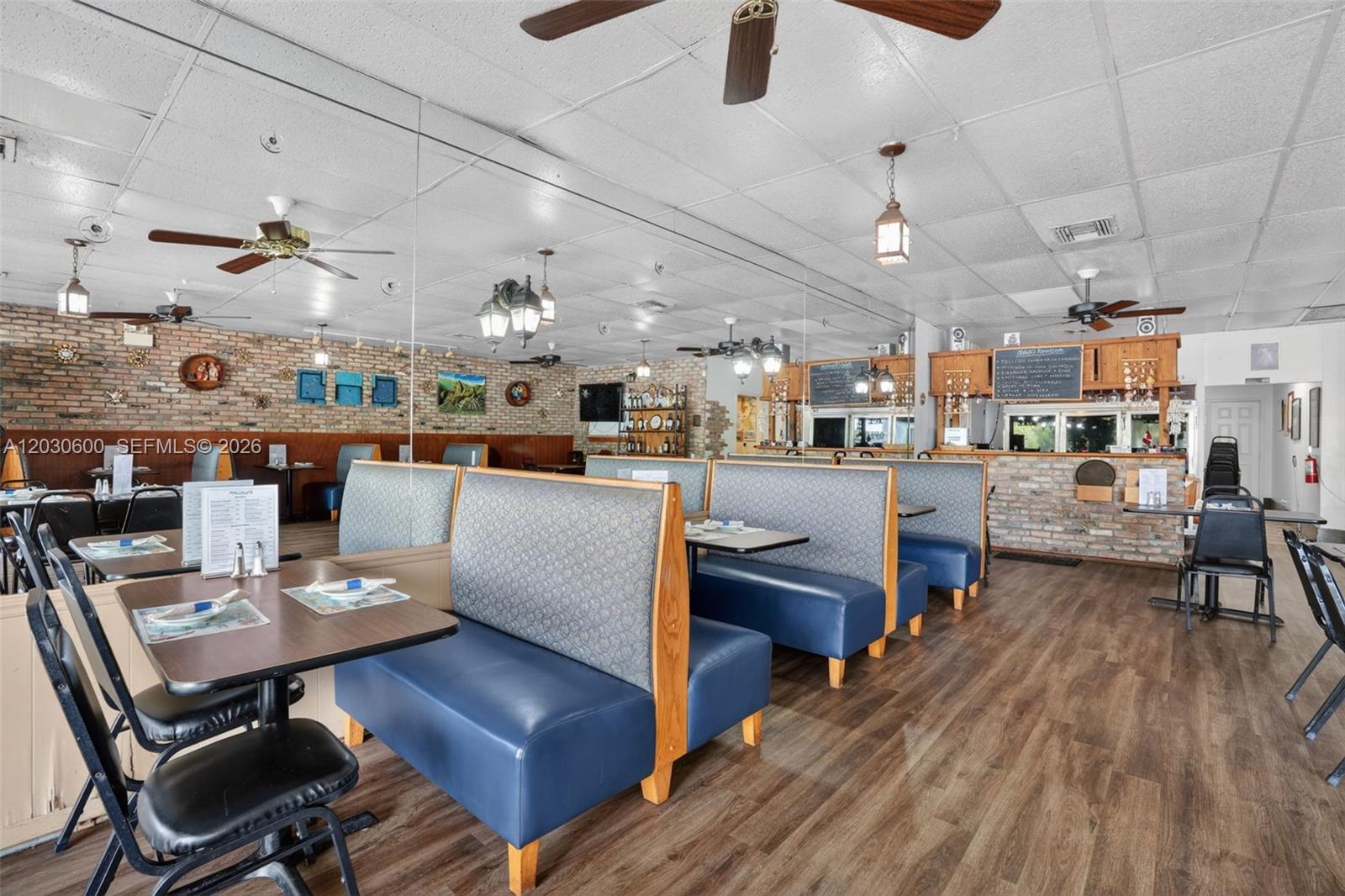 A restaurant interior features blue booths, wooden tables, brick walls, and a drop ceiling — Turnkey Pompano Beach Restaurant, Pompano Beach FL 33060, POMPANO BEACH, FL