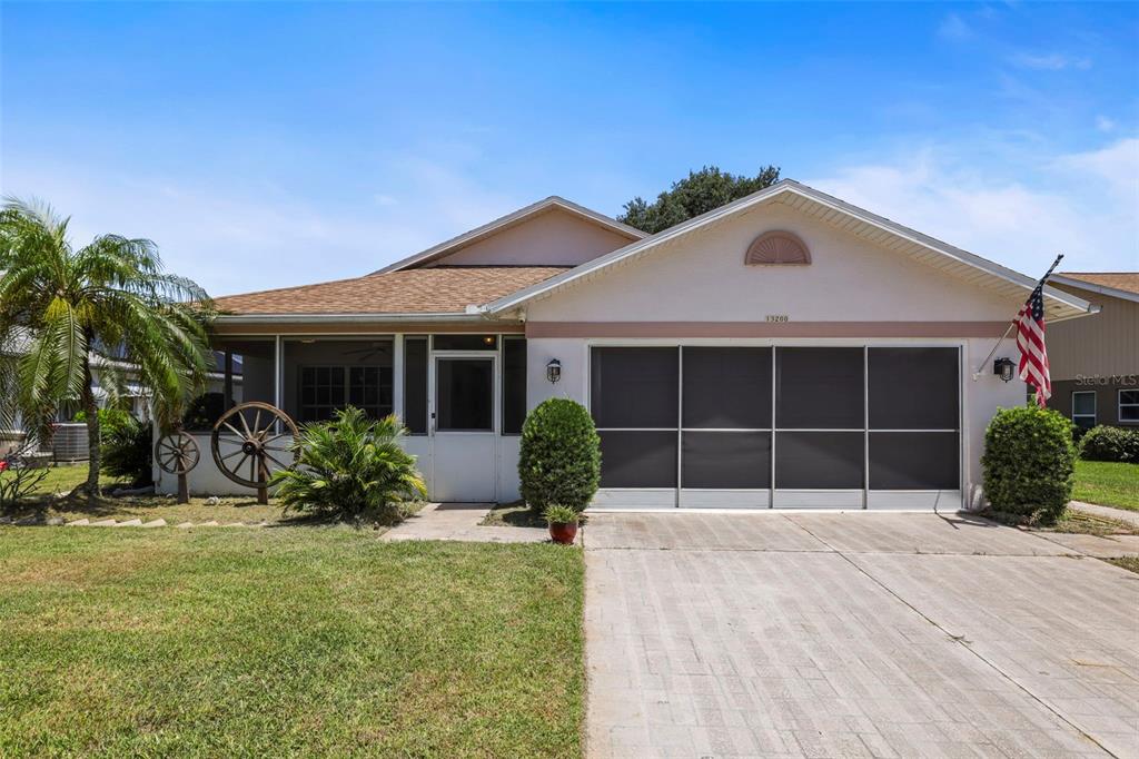 A single-story house features a screened-in front porch, a garage with screen doors, and landscaping — 13200 TITLEIST DRIVE, HUDSON, FL