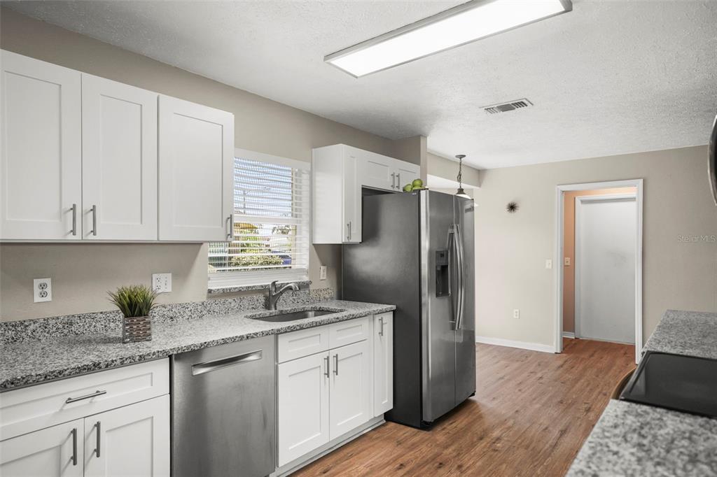 A kitchen with white cabinets, granite countertops, stainless steel appliances, and wood-look flooring — 13200 TITLEIST DRIVE, HUDSON, FL
