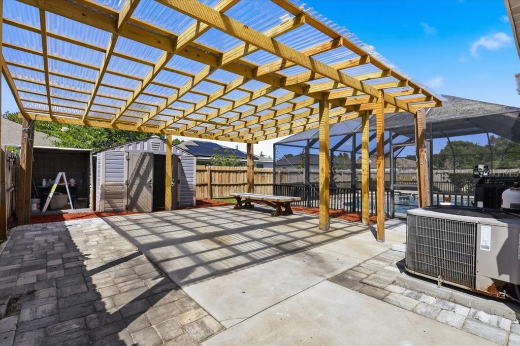 A backyard patio features a wooden pergola with a clear corrugated roof over concrete flooring — 20 BUTTERNUT, PALM COAST, FL