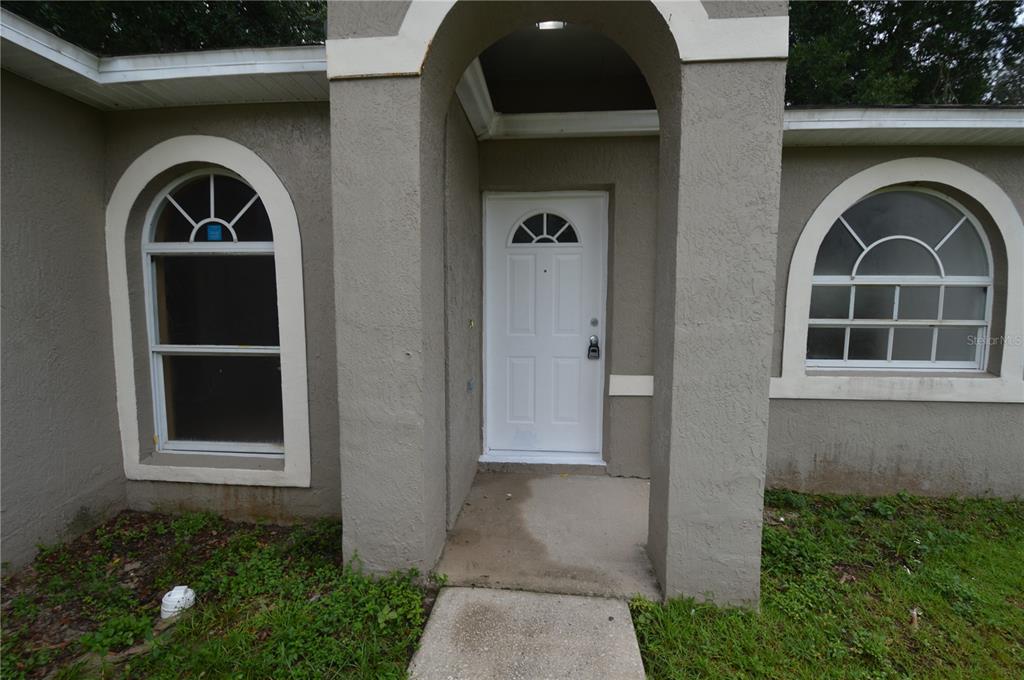 The exterior of a house features a white front door, arched windows, and stucco siding — 622 CARIBOU COURT, POINCIANA, FL