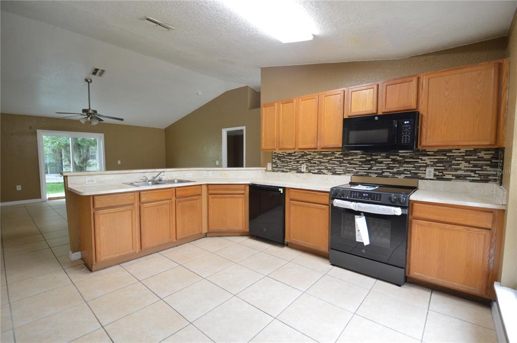 A kitchen with oak cabinets, black appliances, tile flooring, and a tiled backsplash — 622 CARIBOU COURT, POINCIANA, FL