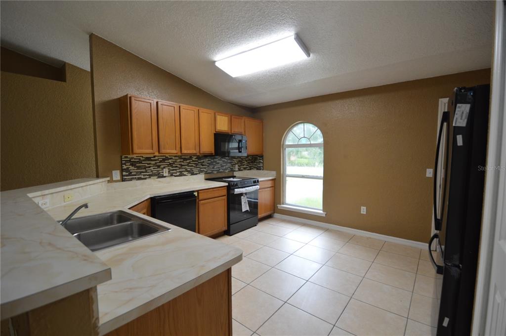 A kitchen features wood cabinets, a tiled backsplash, light countertops, and a black appliance suite — 622 CARIBOU COURT, POINCIANA, FL