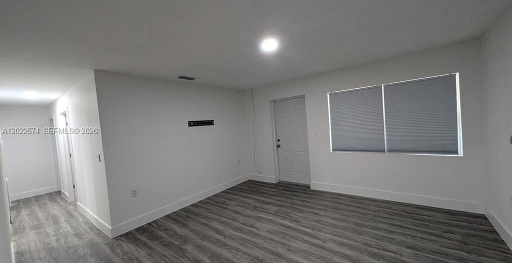 An empty room features white walls, gray wood-look flooring, a white door, and window blinds — 660 S MISSOURI ST, La Belle FL 33935, LA BELLE, FL