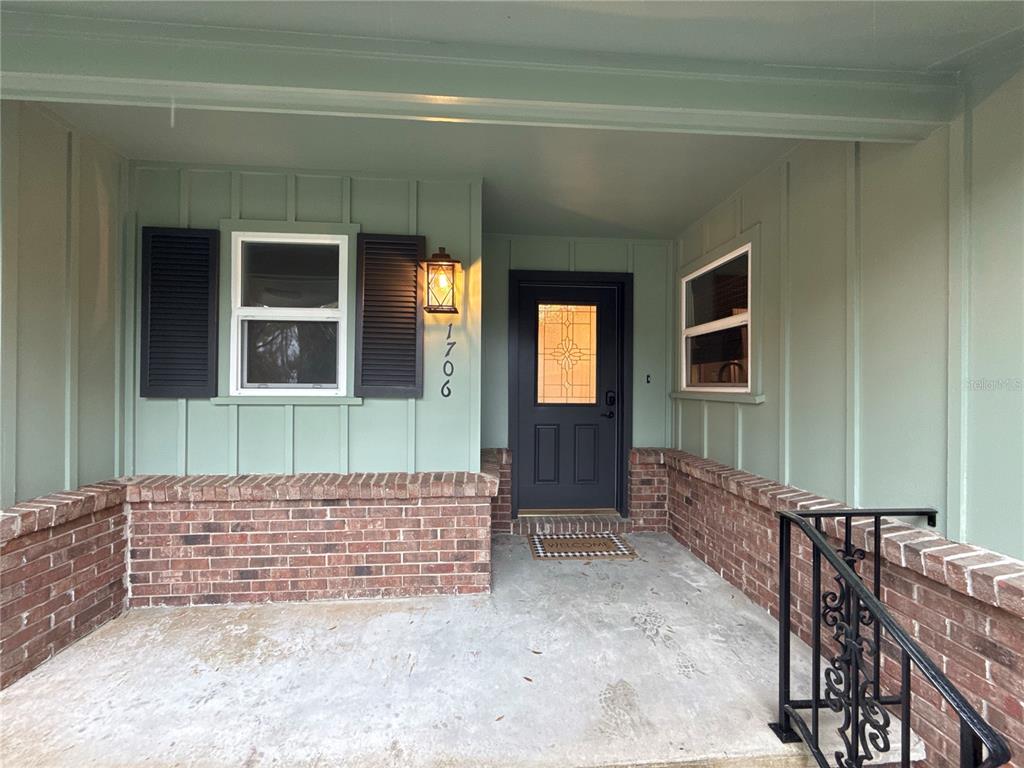 A covered front porch features a dark door, brick walls, and light green vertical siding — 1706 NE 4TH STREET, OCALA, FL