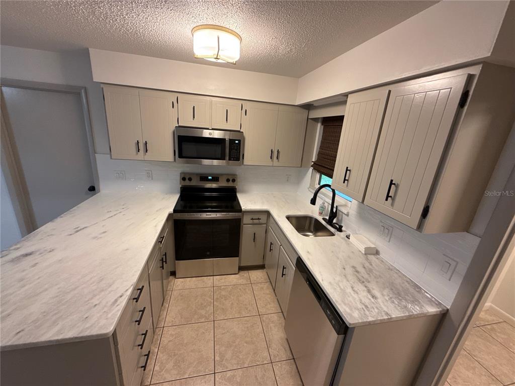 A kitchen features light-colored cabinets, marble-look countertops, stainless steel appliances, and tile flooring — 1706 NE 4TH STREET, OCALA, FL