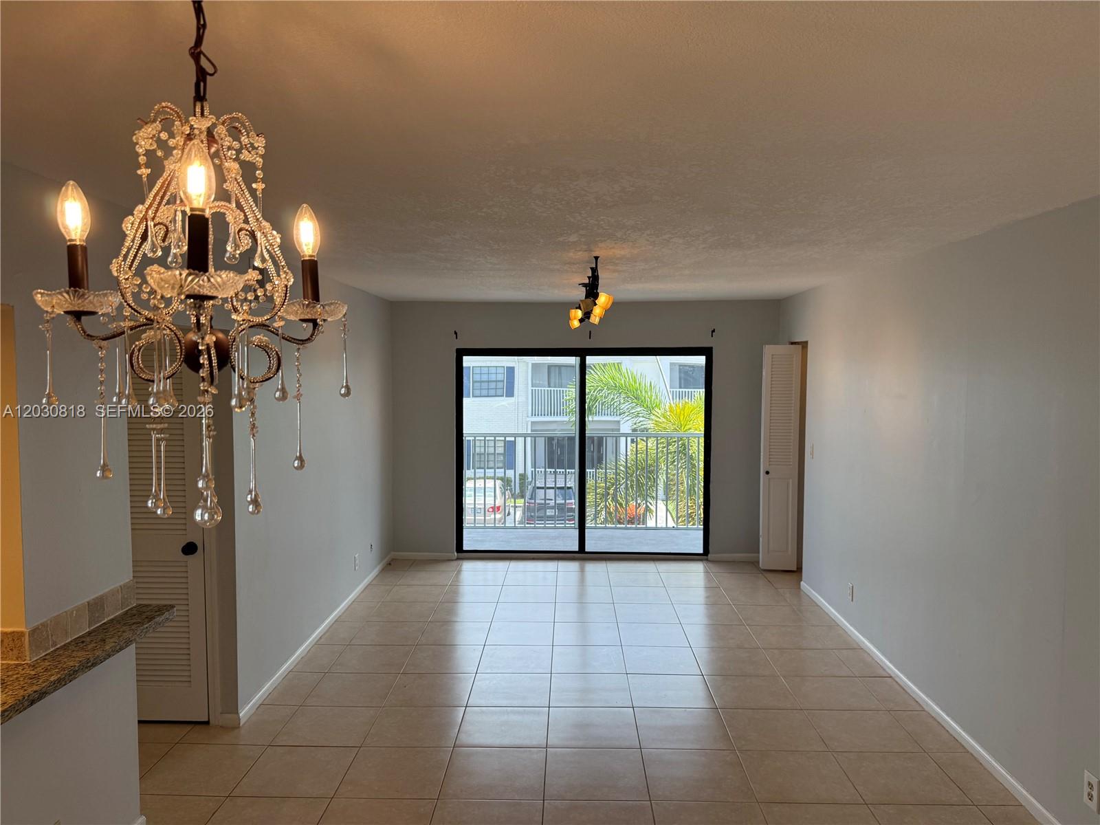An empty living room features tile flooring, a crystal chandelier, and a sliding glass door — 170 Cypress Club Dr # 729, Pompano Beach FL 33060, POMPANO BEACH, FL