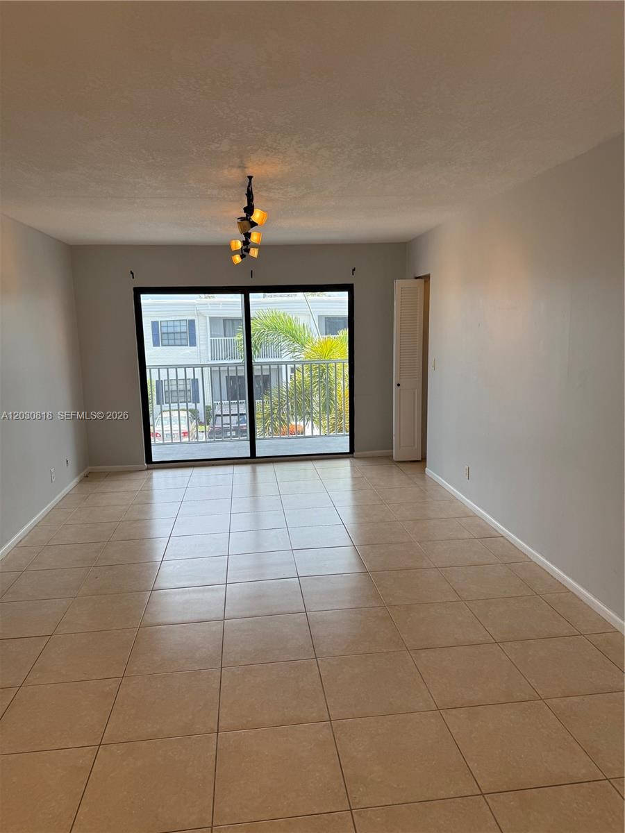 An empty room features light-colored tile flooring, gray walls, a ceiling light, and sliding glass doors — 170 Cypress Club Dr # 729, Pompano Beach FL 33060, POMPANO BEACH, FL