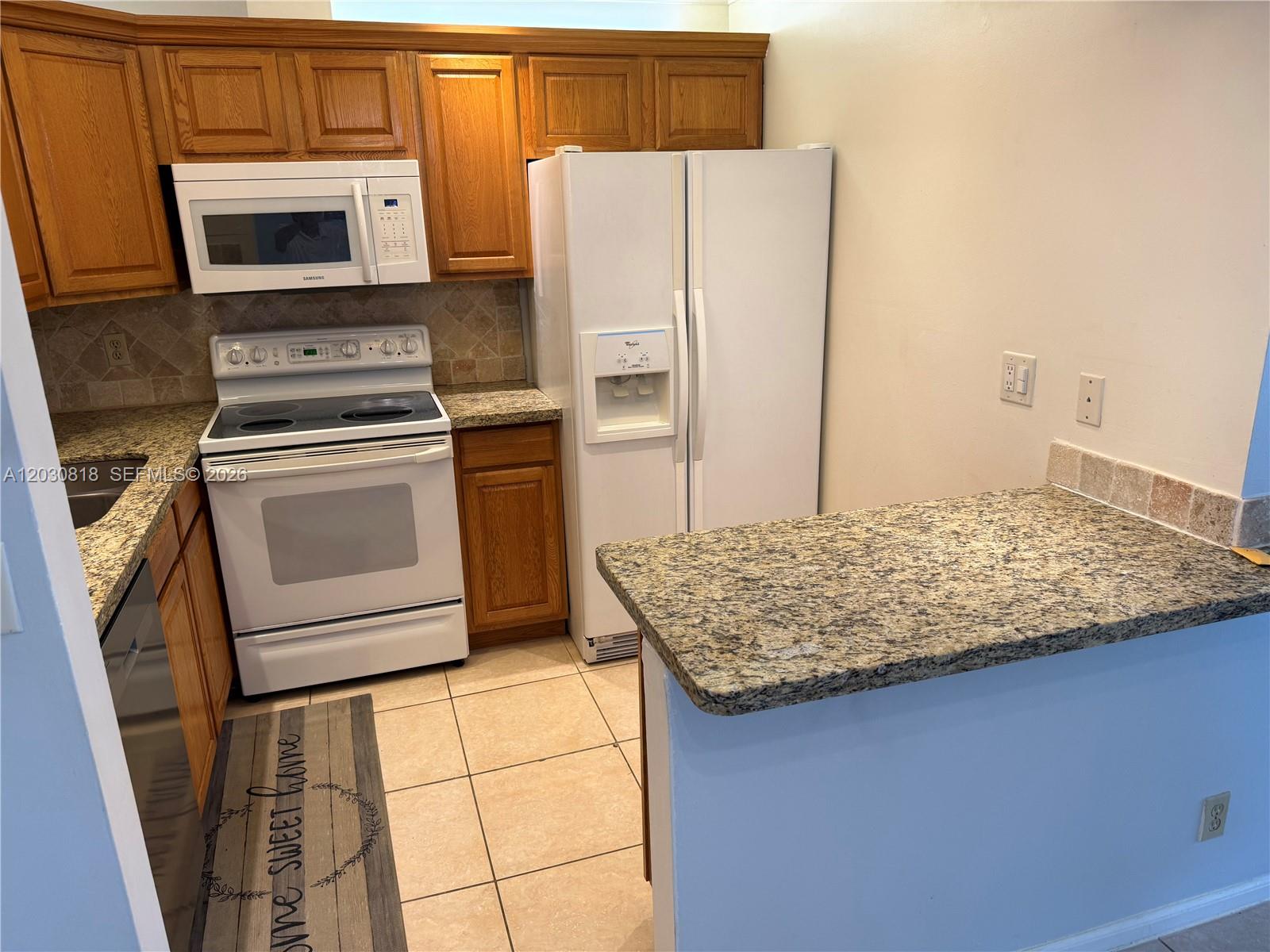 A kitchen features oak cabinets, granite countertops, white appliances, and a tiled floor — 170 Cypress Club Dr # 729, Pompano Beach FL 33060, POMPANO BEACH, FL