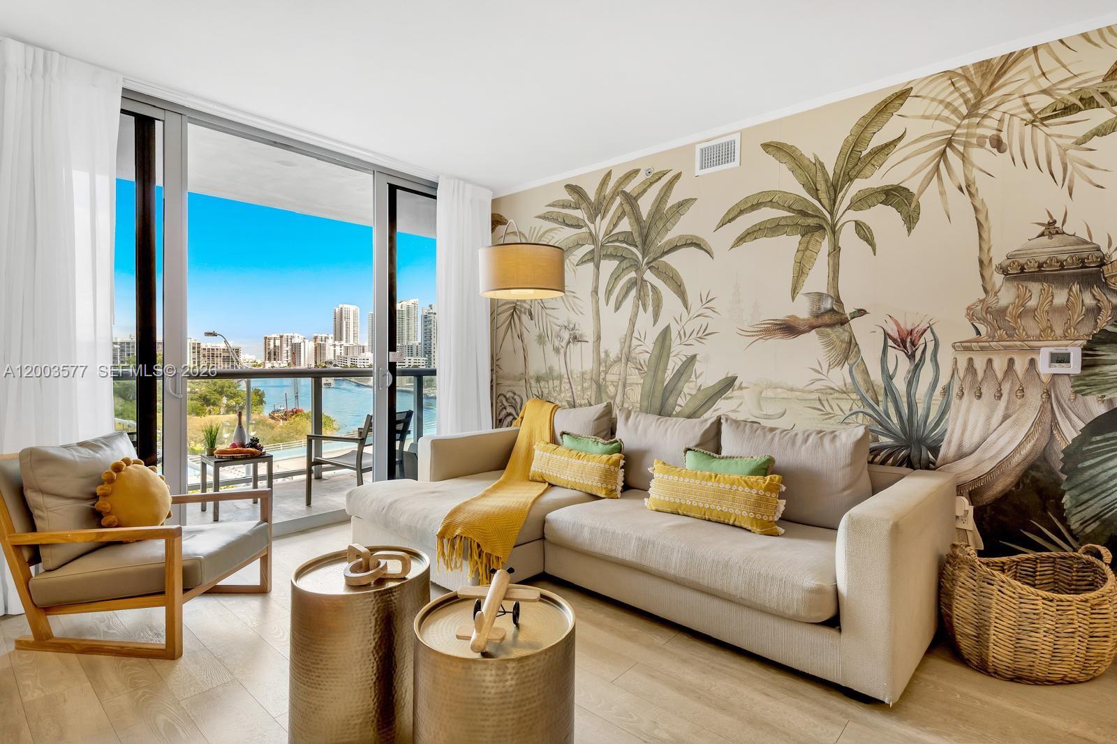 A living room features a tropical mural, a beige sectional sofa, and a balcony view — 2602 E Hallandale Beach Blvd # R704, Hallandale Beach FL 33009, HALLANDALE BEACH, FL