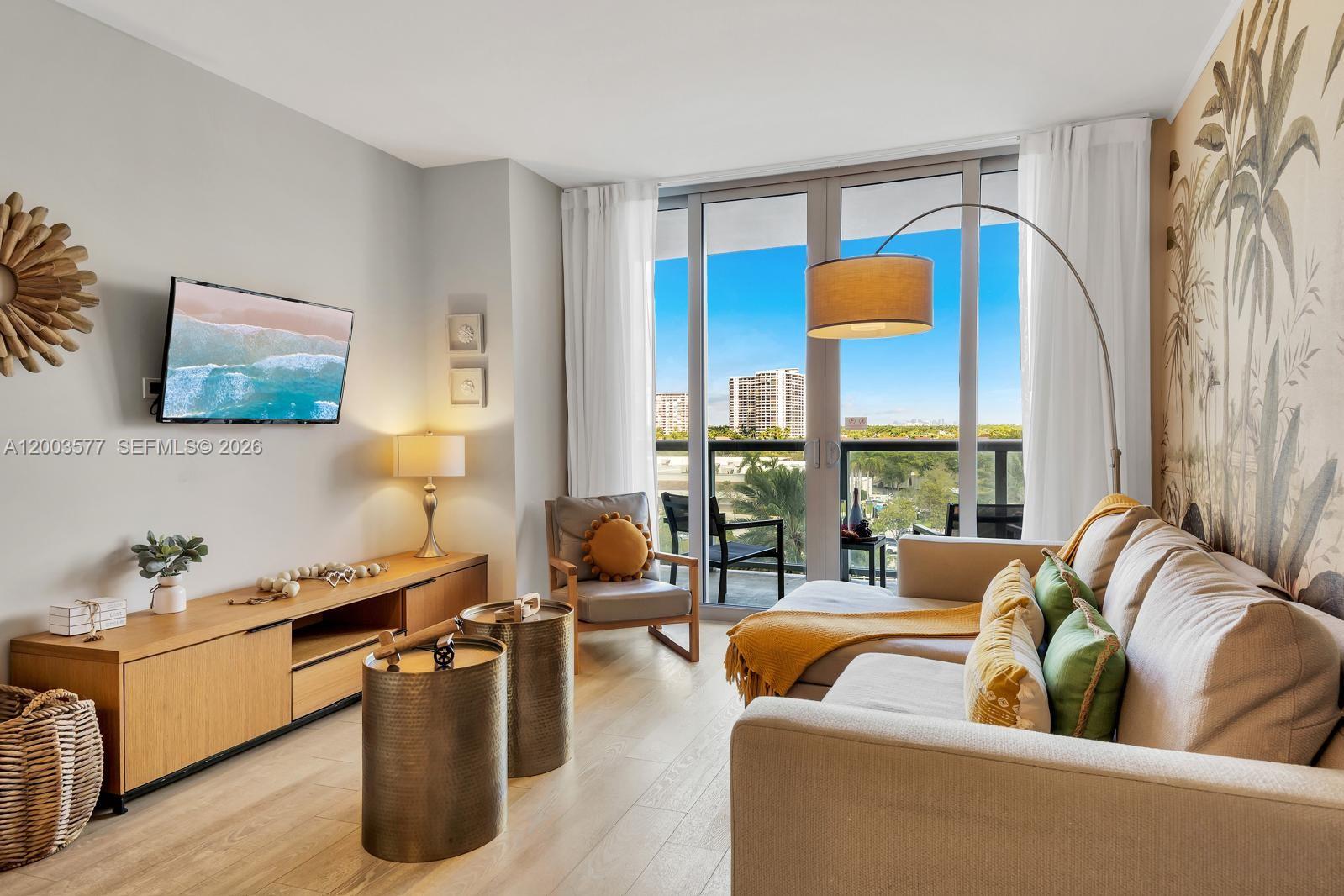 A living room features a sectional sofa, media console, and floor-to-ceiling windows with balcony access — 2602 E Hallandale Beach Blvd # R704, Hallandale Beach FL 33009, HALLANDALE BEACH, FL
