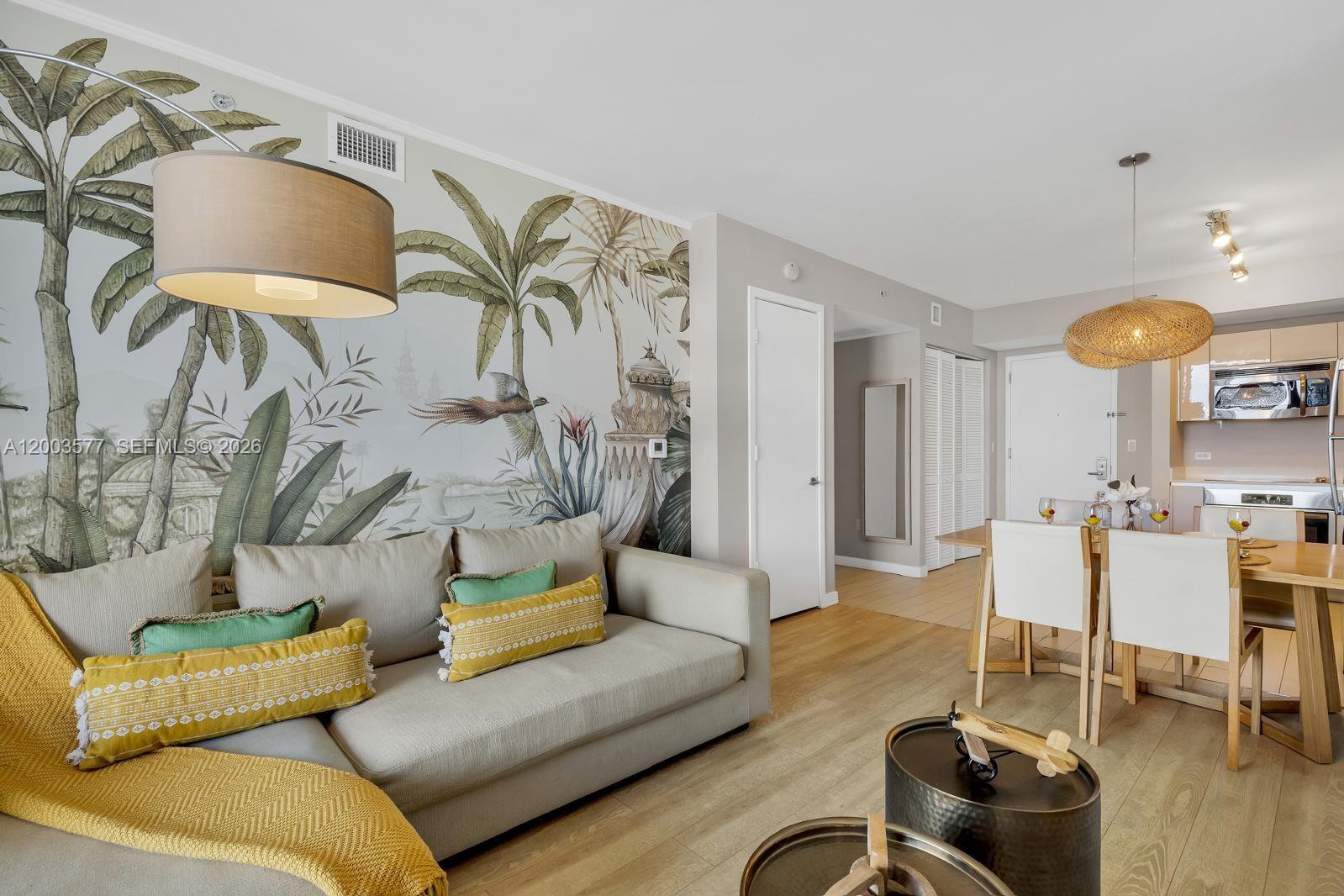 This living and dining area features a tropical mural, light wood flooring, and modern furniture — 2602 E Hallandale Beach Blvd # R704, Hallandale Beach FL 33009, HALLANDALE BEACH, FL