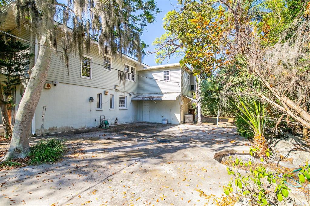 The exterior of a two-story house features light-colored siding, a concrete patio, and surrounding trees — 5013 BAY SHORE ROAD, SARASOTA, FL