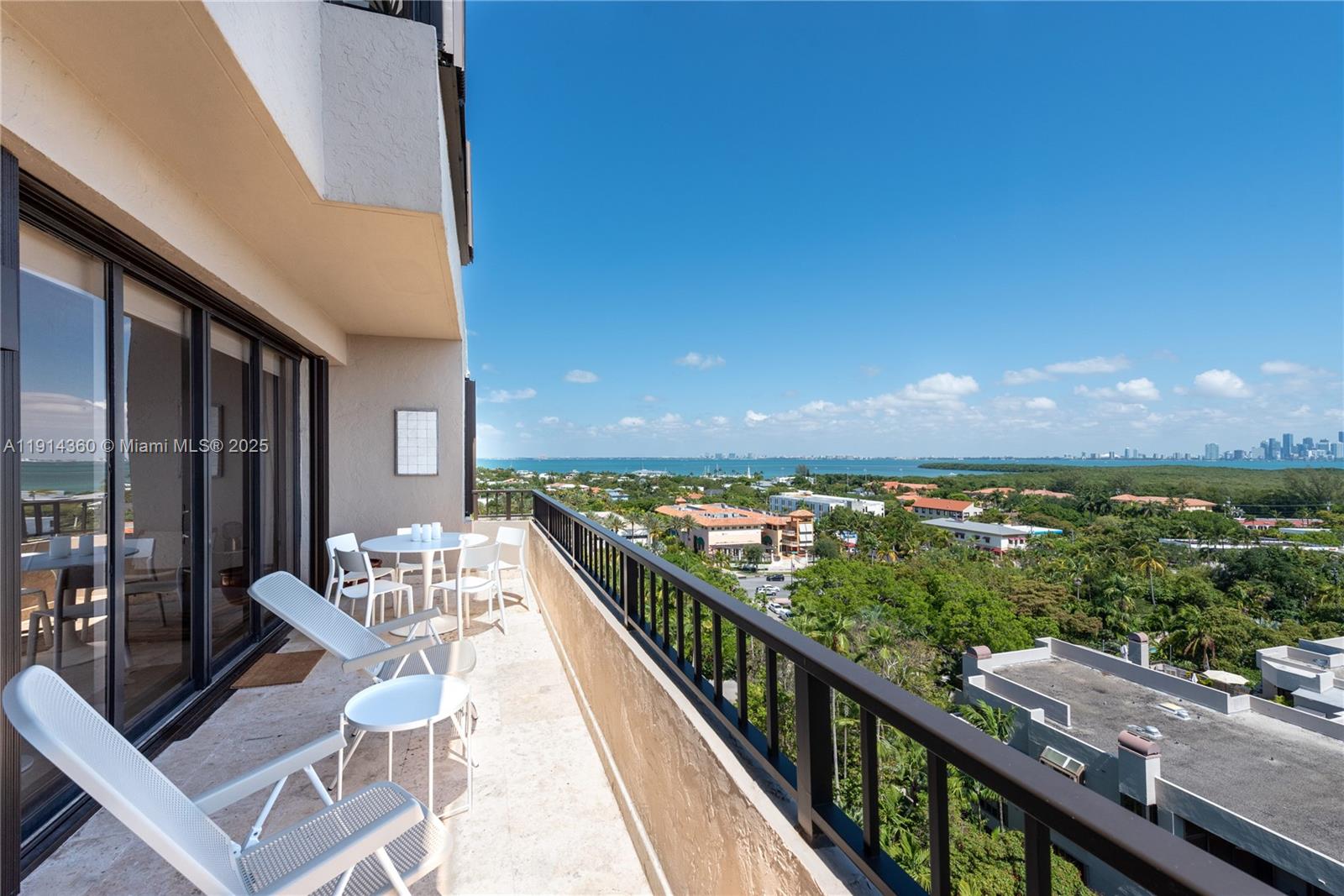 A balcony with white patio furniture overlooks a lush landscape and the distant ocean — 151 Crandon Blvd # 1036, Key Biscayne FL 33149, KEY BISCAYNE, FL