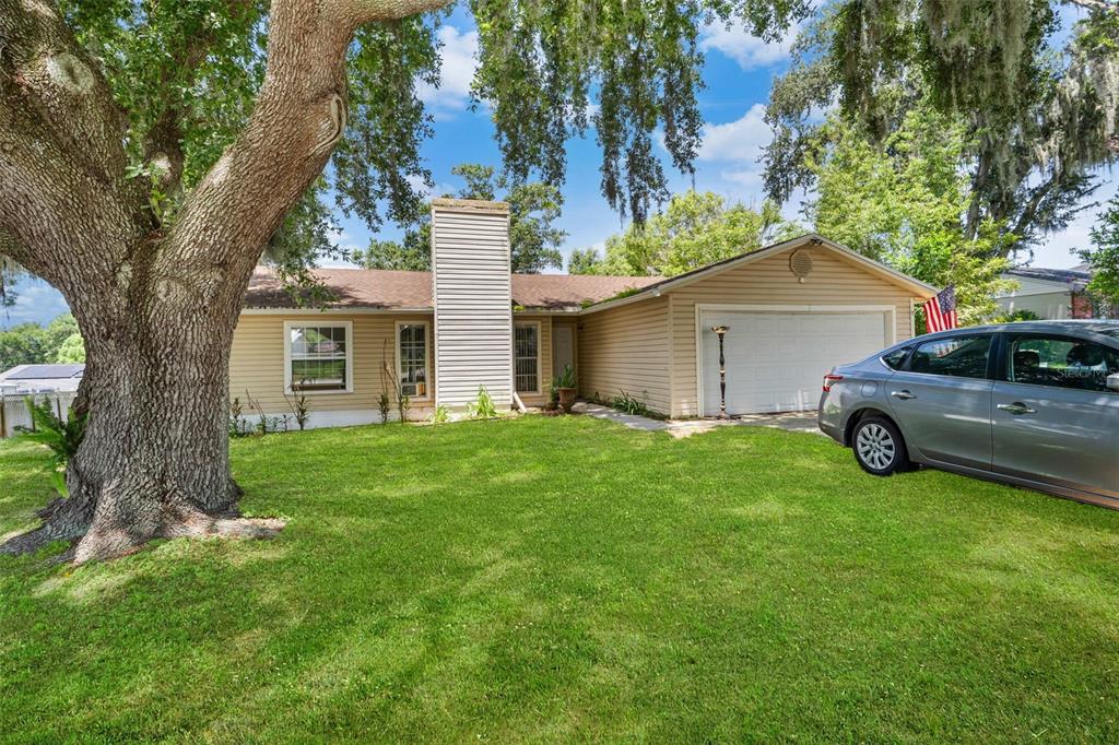 A single-story house with light siding, a chimney, and a large oak tree in front — 7410 ORANGE CREST CIRCLE, LAKELAND, FL