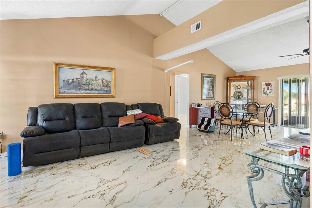 A living room with a large black sofa, marble-look tile flooring, and vaulted ceilings — 7410 ORANGE CREST CIRCLE, LAKELAND, FL
