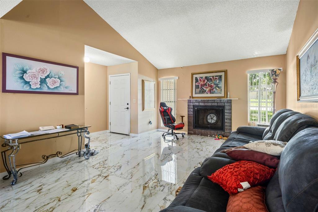 A living room features a fireplace, a dark sofa, and white marble-look tile flooring — 7410 ORANGE CREST CIRCLE, LAKELAND, FL