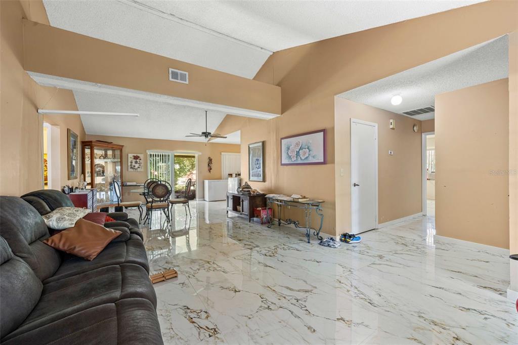 A living room with vaulted ceilings, white marble-look tile flooring, and tan walls — 7410 ORANGE CREST CIRCLE, LAKELAND, FL