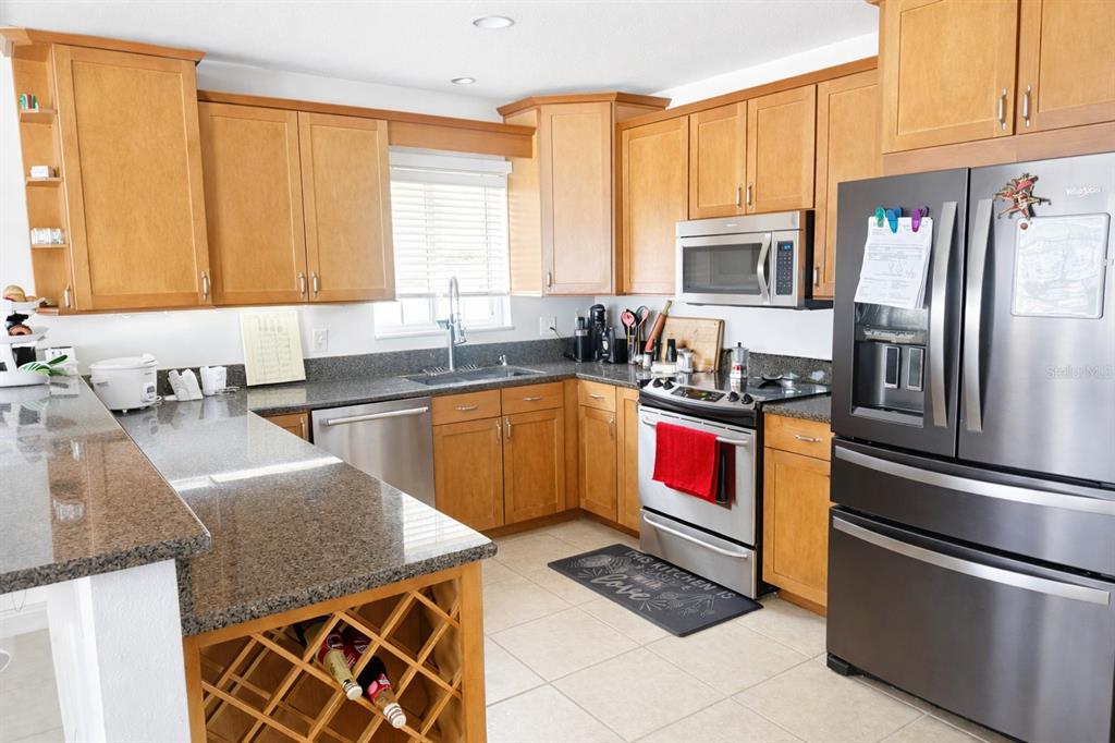 A kitchen features light wood cabinets, granite countertops, stainless steel appliances, and a wine rack — 3520 STABLE RIDGE LANE, LAND O LAKES, FL