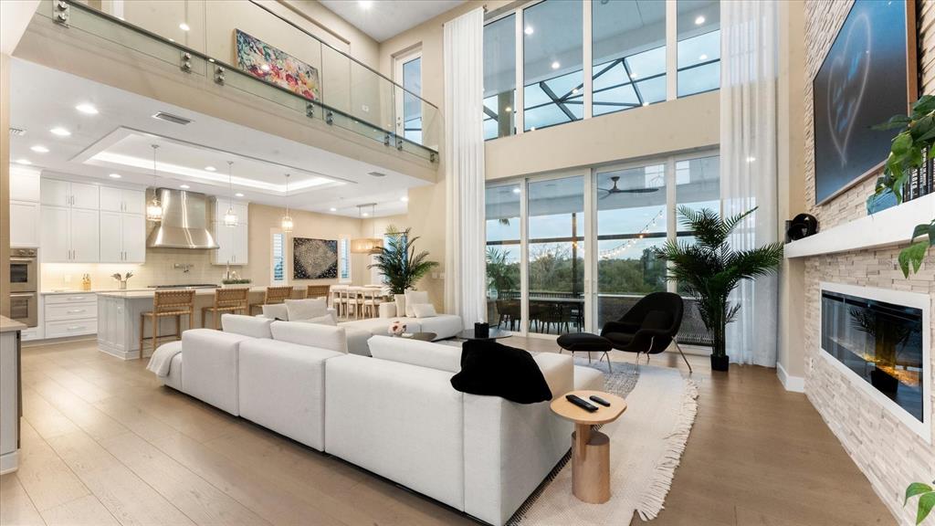 A spacious open-concept living room features a white sectional, fireplace, and floor-to-ceiling windows — 5708 INSPIRATION TERRACE, BRADENTON, FL