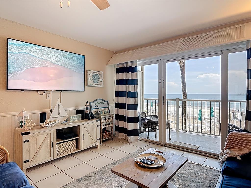 A living room with a television, beach-themed decor, and a balcony overlooking the ocean — 4849 SAXON DRIVE UNIT A204, NEW SMYRNA BEACH, FL