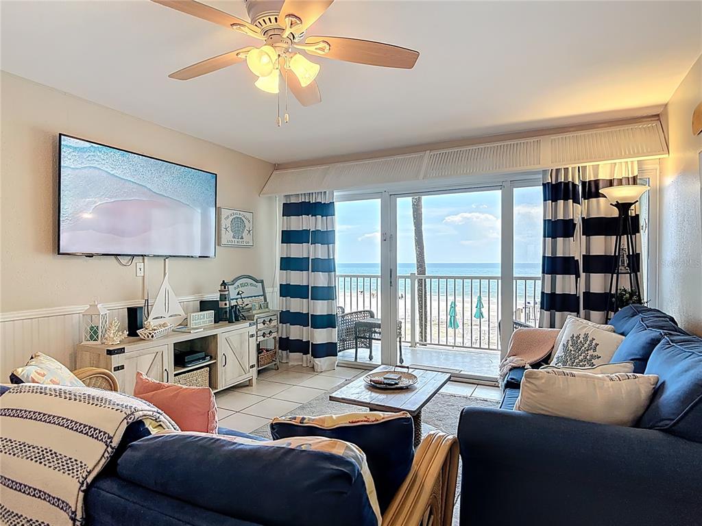 A living room features a blue sofa, a television, and a balcony overlooking the ocean — 4849 SAXON DRIVE UNIT A204, NEW SMYRNA BEACH, FL
