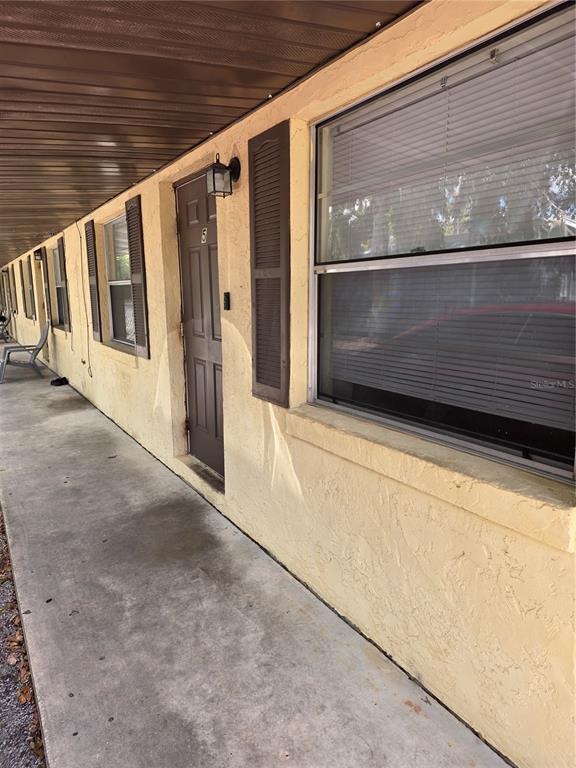 A concrete walkway runs along the exterior of a yellow building with brown shutters — 830 N CLAKE STREET UNIT 1, DELAND, FL