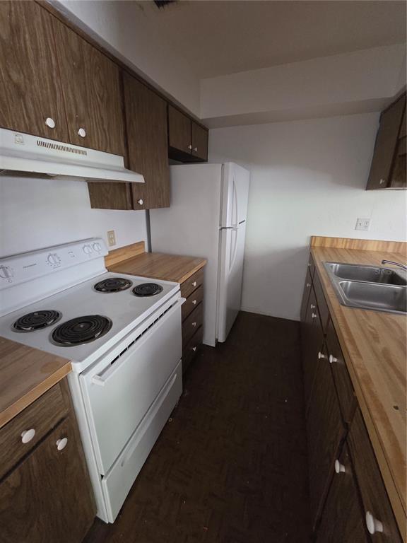 A galley-style kitchen features wood cabinets, laminate countertops, white appliances, and dark flooring — 830 N CLAKE STREET UNIT 1, DELAND, FL