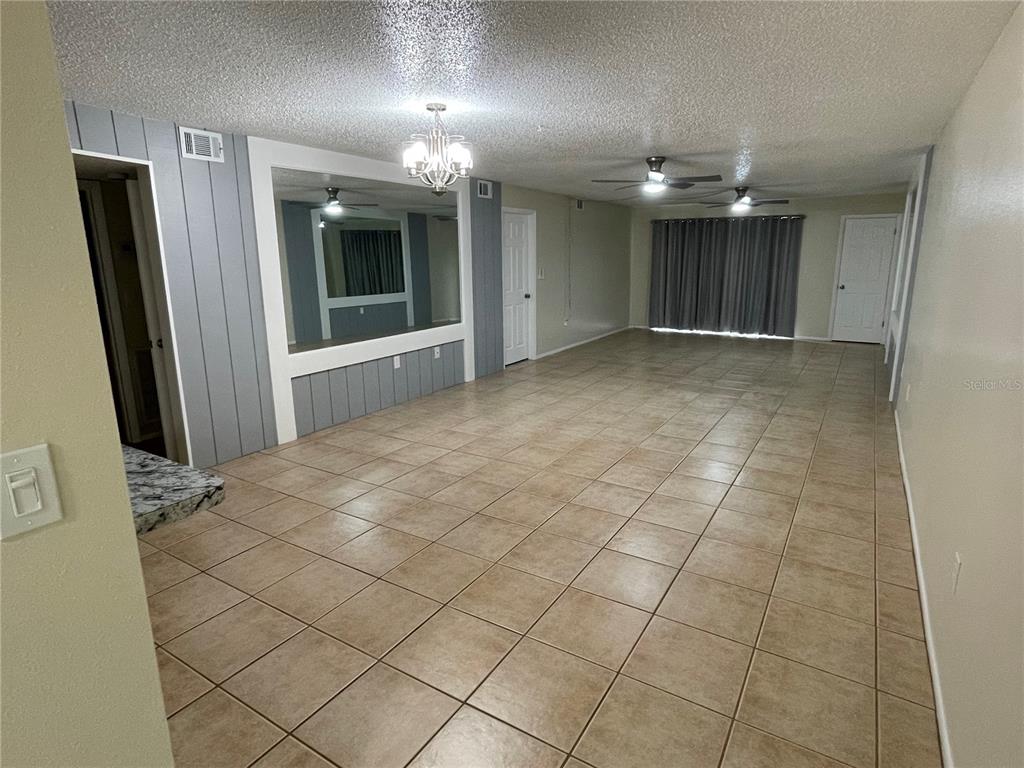A large, tiled living room features a mirrored wall, two ceiling fans, and a chandelier — 7640 92ND STREET UNIT 101E, SEMINOLE, FL