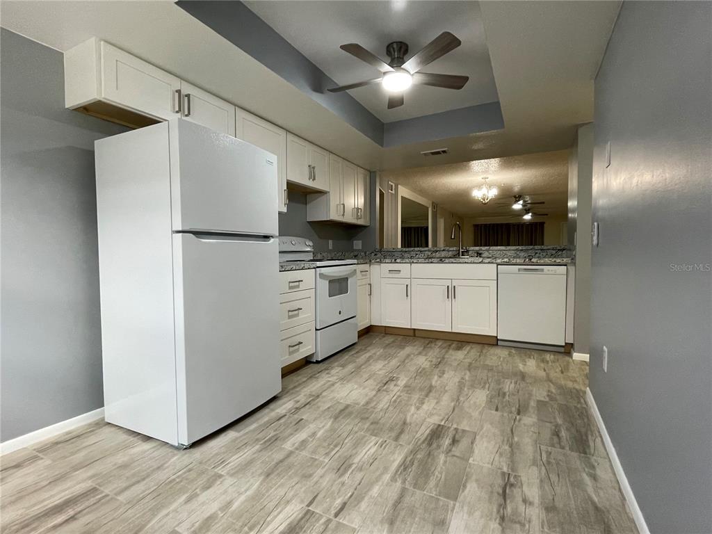 A kitchen features white cabinets, white appliances, gray walls, and light wood-look flooring — 7640 92ND STREET UNIT 101E, SEMINOLE, FL