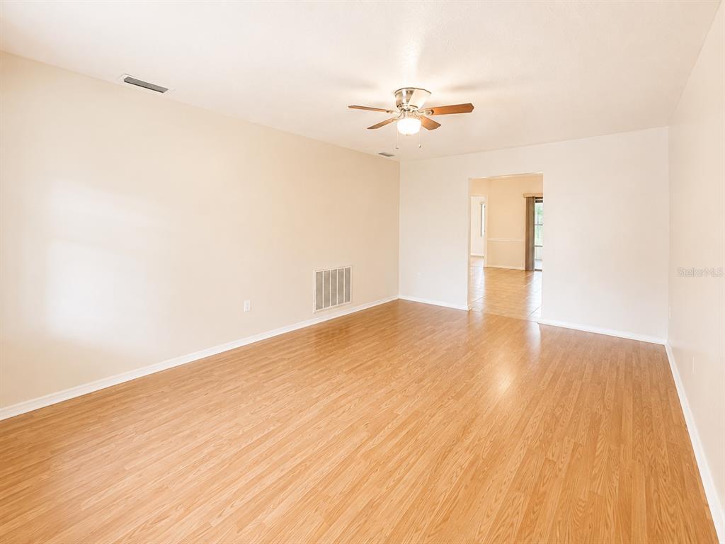 An empty living room features light wood-look flooring, beige walls, and a ceiling fan — 3524 BRISTOL STREET, SEBRING, FL