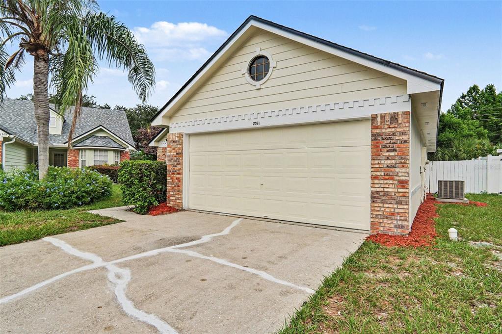 A beige house exterior features a two-car garage, brick accents, and a cracked concrete driveway — 2361 ROANOKE COURT, LAKE MARY, FL