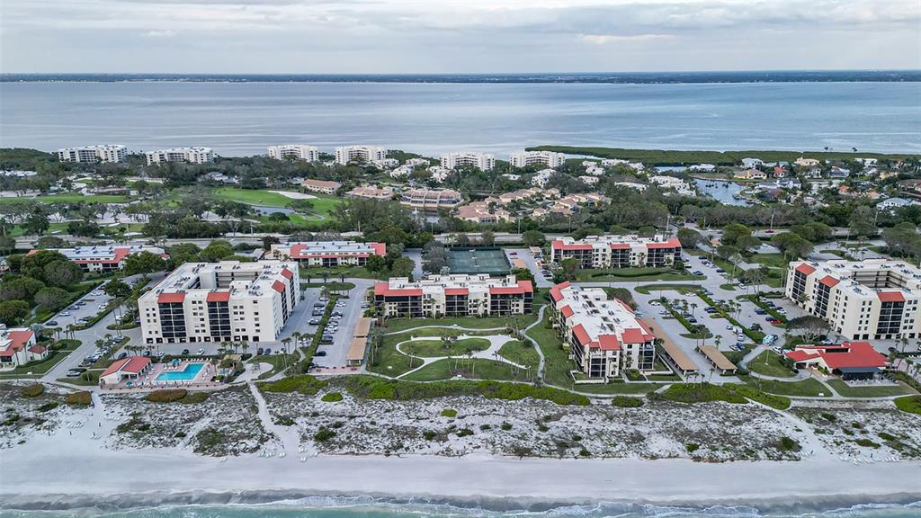 An aerial view shows several multi-story condominium buildings situated along a sandy beach — 1975 GULF OF MEXICO DRIVE UNIT 208, LONGBOAT KEY, FL