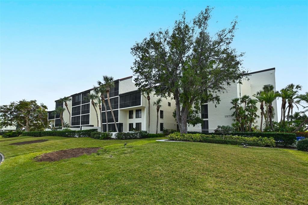 A multi-story apartment building with screened balconies sits behind a large, grassy lawn — 1975 GULF OF MEXICO DRIVE UNIT 208, LONGBOAT KEY, FL