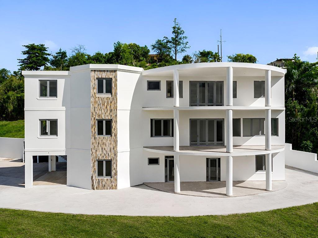 A three-story modern white house with a curved facade, stone accents, and wrap-around balconies — CARR 171 MOGOTE, CAYEY, PR