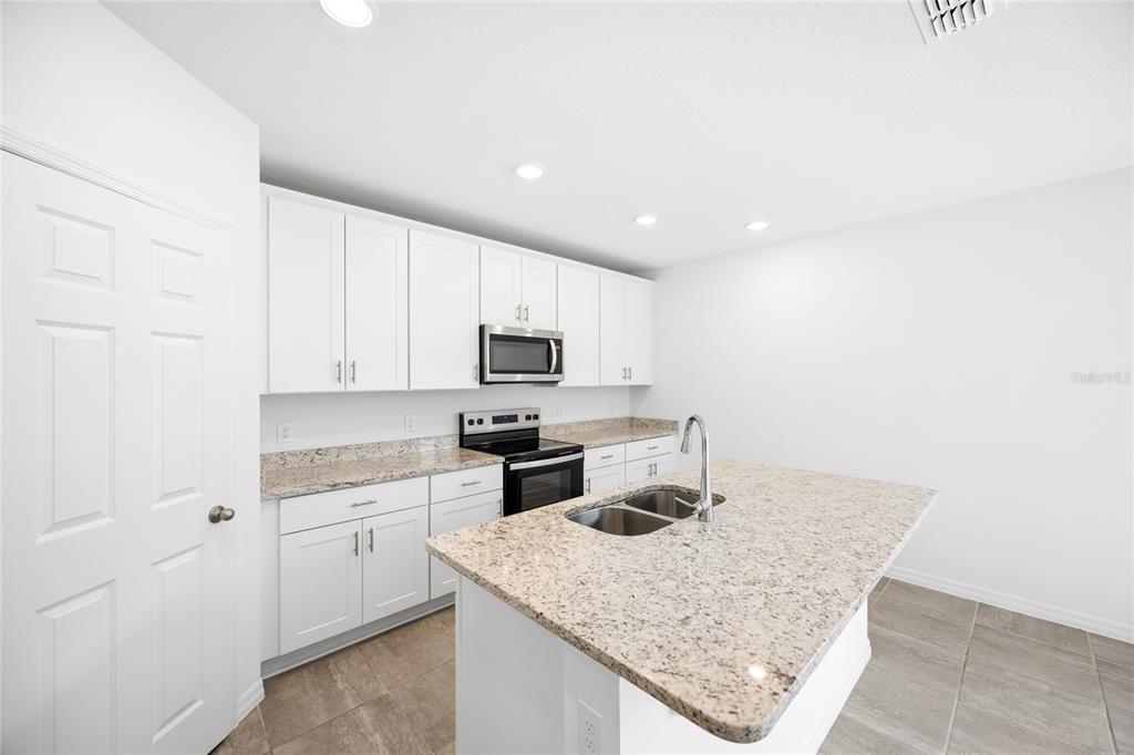 A kitchen features white cabinets, granite countertops, a center island with a sink, and appliances — 2339 WHITE TAIL, DAVENPORT, FL