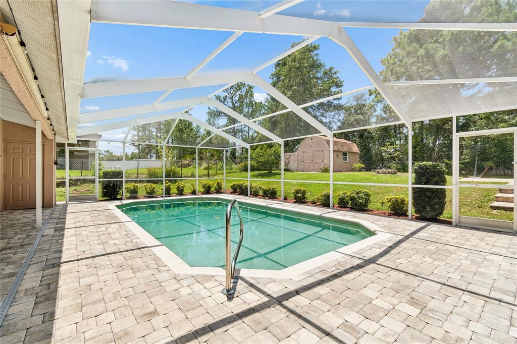 A screened-in swimming pool with a paver patio and a backyard shed in the distance — 8293 NITTANY ROAD, WEEKI WACHEE, FL