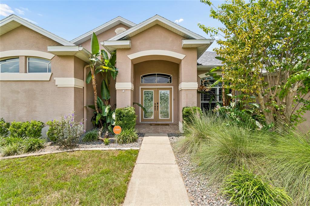 A tan stucco house features a covered entryway with double glass doors and landscaping — 8293 NITTANY ROAD, WEEKI WACHEE, FL