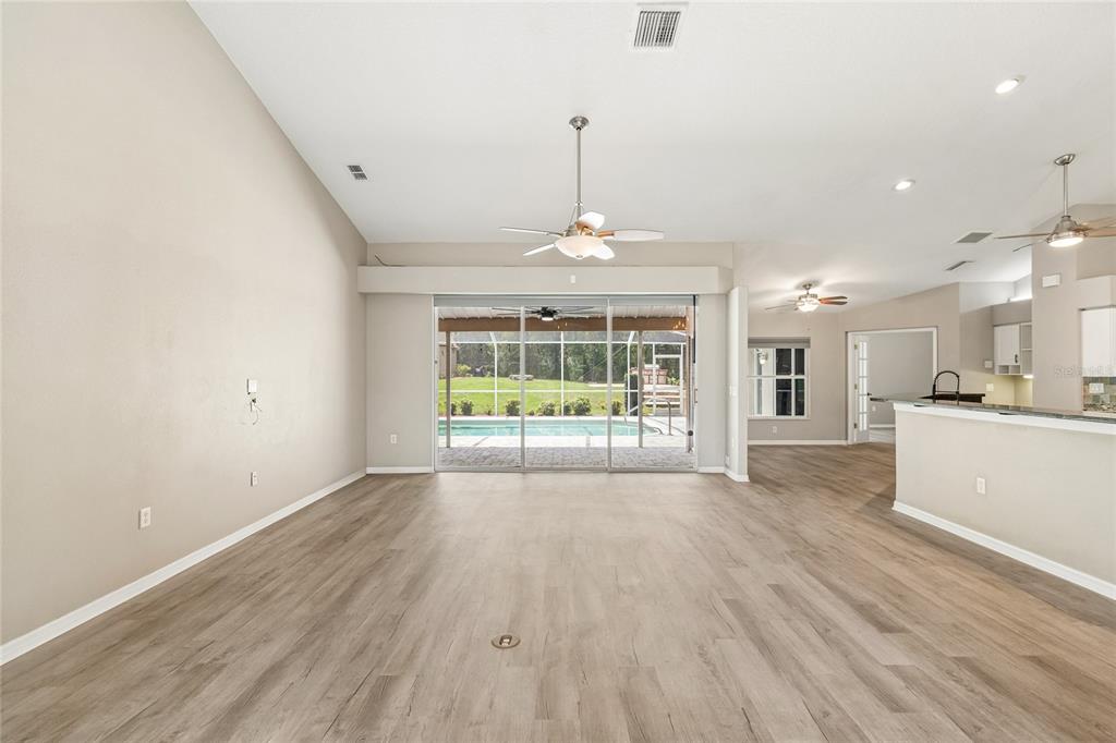 A spacious living room with light wood flooring, a ceiling fan, and sliding glass doors — 8293 NITTANY ROAD, WEEKI WACHEE, FL