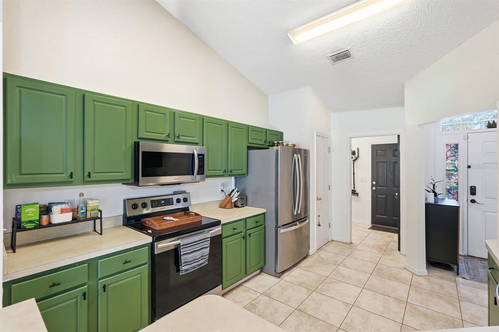 A kitchen features green cabinets, stainless steel appliances, and light-colored tile flooring — 36 LEMA LANE, PALM COAST, FL