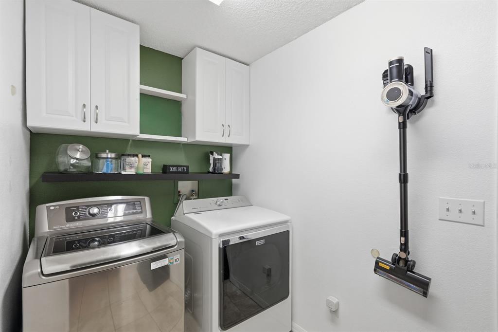 A laundry room features white cabinets, a green accent wall, and a mounted cordless vacuum — 36 LEMA LANE, PALM COAST, FL